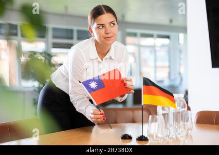 Vorbereitung auf Geschäftsverhandlungen - Frau setzt kleine Flaggen von Taiwan und Deutschland auf den Tisch Stockfoto