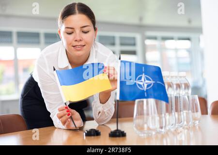 Geschäftsfrau, die die Flaggen der NATO und der Ukraine für Präsentationen und Verhandlungen arrangiert Stockfoto