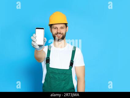 Professioneller Mechaniker in Uniform, der das Smartphone auf hellblauem Hintergrund zeigt Stockfoto