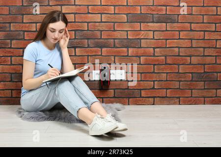 Frau sitzt auf dem Boden, während sie die elektrische Heizung in Innenräumen auflädt, Platz für Text Stockfoto