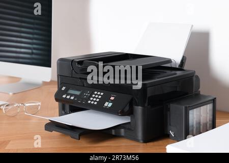 Moderner Drucker mit Papier in der Nähe des Computers auf einem Holztisch im Büro Stockfoto
