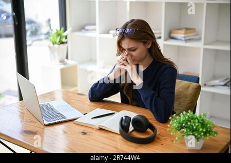 Eine gestresste, ängstliche und aufmerksame junge asiatische Geschäftsfrau, die unter Überarbeit leidet, ihrer Arbeit müde ist und versucht, die Solutio zu verstehen Stockfoto