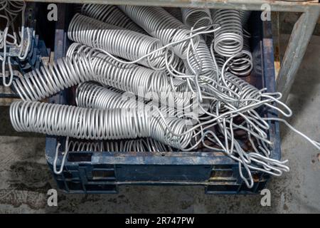 Graue Drähte, zu einer Spirale verdrillt, Federn in einer Box. Produktion, Lagerung von Elektrodrähten. Eine Drahtspule. Stapel Eines verwickelten langen Schlauchs oder eines Kabeldrahts Stockfoto