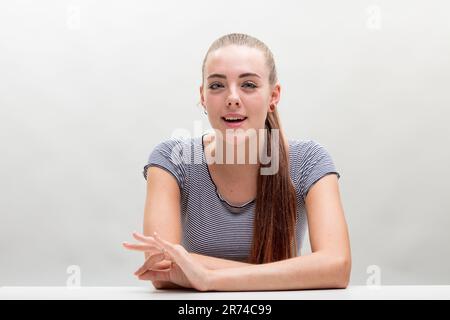 Frontales Porträt einer jungen Frau, gestreiftes Hemd, gefesselte Haare, mitten in der Rede und Gesten gefangen. Sie macht das "OK" -Zeichen, lebhaft und lächelnd, begeistert Stockfoto