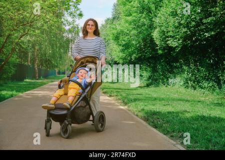 Das Kind und die Mutter machen einen gemütlichen Spaziergang durch den Park mit ihrer Kutsche. Kind im Alter von etwa zwei Jahren (ein Jahr und elf Monate) Stockfoto