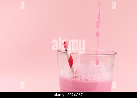 Gestreiftes Stroh in einem Glas Erdbeermilchshake, isoliert auf rosa Stockfoto