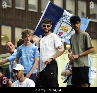 Manchester, Großbritannien. 12. Juni 2023.man City-Fans standen auf einer Baustelle, um die Siegesparade mit offenem Oberdeck im Zentrum von Manchester, Großbritannien, zu sehen, um die Erfolge ihres Clubs zu feiern, der die Höhen gewonnen hat: Die Premier League, der FA Cup und die Champions League. Am Samstag besiegte man City Inter Mailand in Istanbul und sicherte sich den Champions League-Sieg. Die Parade der offenen Busse fuhr durch das Stadtzentrum von Manchester und beobachtete von großen, begeisterten Massen, trotz Gewitter und starkem Regen. Kredit: Terry Waller/Alamy Live News Stockfoto