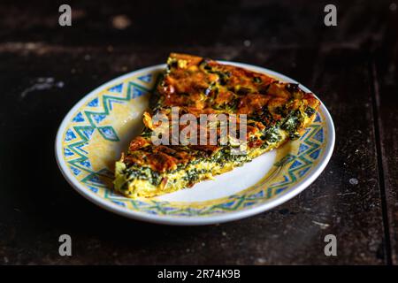 Ein Stück frisch zubereiteter Spinat- und Käsekuchen auf einem Teller mit dunklem Hintergrund. Veganischer Kuchen. Stockfoto