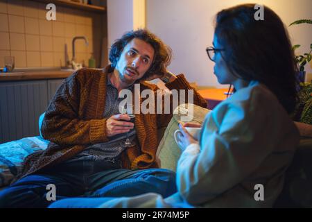 Ein junges Paar verbringt abends Zeit zu Hause auf der Couch. Mann und Frau sprechen über Geschäfts- und Beziehungsprobleme. Stockfoto