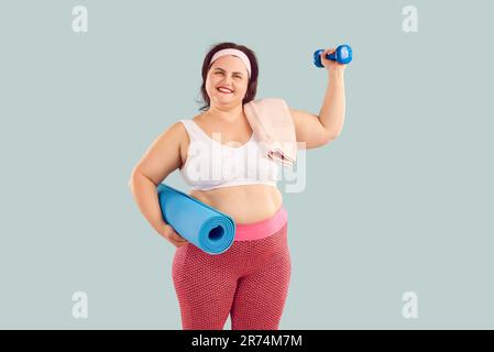 Porträt einer glücklichen, dicken, übergewichtigen jungen Frau mit Kurzhantel und Fitnessmatte Stockfoto