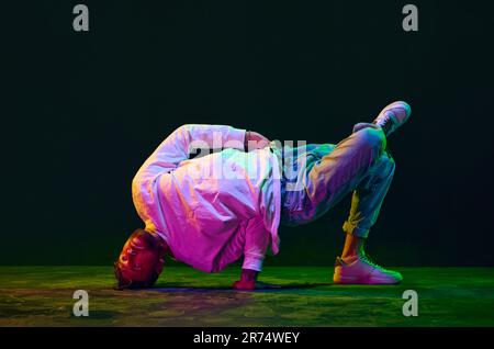 Flexibilität. Junger Mann in sportlicher Kleidung tanzt Hip-Hop, Breakdance vor schwarzem Studiohintergrund in Neonlicht Stockfoto