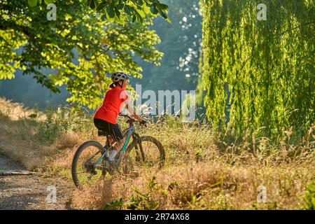 Attraktive Seniorin, die mit ihrem elektrischen Mountainbike im Stadtpark Stuttgart, Baden-Württemberg, fährt Stockfoto