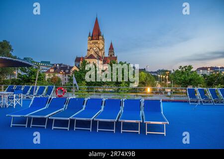 Sonnenliegen auf dem Oberdeck mit der Kirche St. Franziskus von Assisi an der Donau, Wien, Österreich Stockfoto