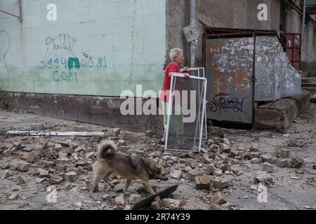 KHERSON, UKRAINE - 12. Juni 2023: Chaos und Zerstörung auf den Straßen von Kherson. Ein streunender Hund und eine Frau werden dabei gesehen, wie sie ihre Habseligkeiten retten. Stockfoto