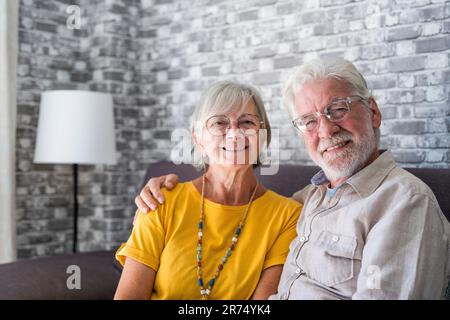 Wunderschöne, gut aussehende, reife Ehepartner, die sich auf der bequemen Couch im modernen Heim entspannen und die Kamera anstarren, fühlen sich sorgenfrei. Gute harmonische Beziehungen, glückliche Ehe, endloses Liebeskonzept Stockfoto