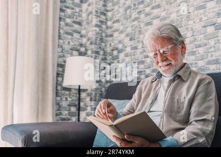 Porträtaufnahme des alten glücklichen und entspannten Mannes, der zu Hause ein Buch liest. Ein erwachsener Mann genießt Freizeit und Spaß im Haus. Stockfoto