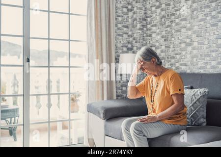 Traurige depressive Frau mittleren Alters, die allein zu Hause sitzt und den Kopf berührt Migräne, verärgerte alte Seniorin Witwe Trauer leiden unter Trauer Einsamkeit psychische Probleme Konzept Stockfoto