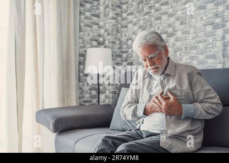 Besorgter älterer älterer Mann fühlt sich schlecht, verärgert alter Großvater mittleren Alters berührt Brust plötzliche Schmerzen Sodbrennen hat Herzinfarkt zu Hause auf dem Sofa sitzen Stockfoto