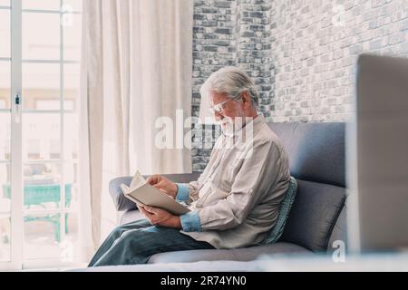 Porträtaufnahme des alten glücklichen und entspannten Mannes, der zu Hause ein Buch liest. Ein erwachsener Mann genießt Freizeit und Spaß im Haus. Stockfoto