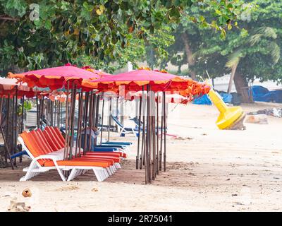 Strand in Pattaya, Thailand mit leeren Liegen und einer gelben Boje im Hintergrund am Strand gestrandet. Bäume über den Sonnenschirmen und im Rücken Stockfoto