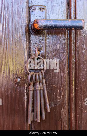 Alter rostiger Schlüssel im Schlüsselloch einer braunen Holztür, Stockfoto