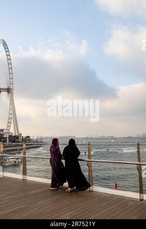2023. Mai 5, Dubai, Vereinigte Arabische Emirate.Blaue Wasserinsel. Frauen in langen Kleidern und Kopftüchern bewundern den Sonnenuntergang bei windigem Wetter Stockfoto