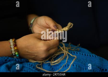 Die Hände einer Frau und Jutefaden und ein Stück Strickmuster. Natürliches umweltfreundliches Stricken, Basteln und Hobby, umweltfreundliche Inneneinrichtung. Stockfoto