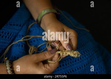 Die Hände einer Frau und Jutefaden und ein Stück Strickmuster. Natürliches umweltfreundliches Stricken, Basteln und Hobby, umweltfreundliche Inneneinrichtung. Stockfoto