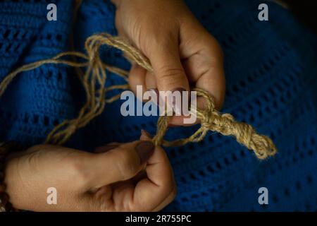 Die Hände einer Frau und Jutefaden und ein Stück Strickmuster. Natürliches umweltfreundliches Stricken, Basteln und Hobby, umweltfreundliche Inneneinrichtung. Stockfoto