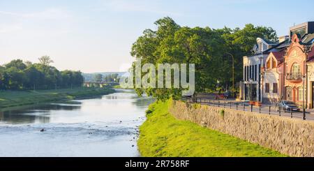 Stadtbild mit Fluss uzh. Ufer der Innenstadt mit alten Gebäuden am anderen Ufer in der Ferne. Sonniger Sommermorgen Stockfoto
