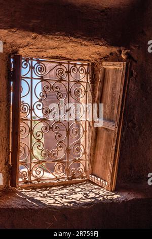 Ein kunstvoll verziertes Fenstergitter und verfallene Holzläden in einer typischen marokkanischen Kasbah Stockfoto