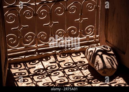 Schatten eines typischen kunstvoll verzierten Fenstergitters, das auf einen Stein fällt, eine Kasbah an der Straße der Kasbahs, Marokko Stockfoto