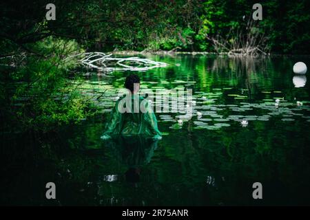 Nicht binäre Person mit grünem Tuch in einem Teich Stockfoto