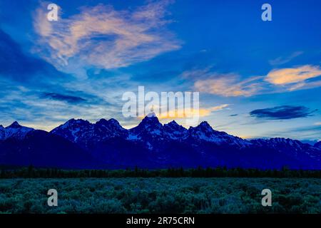 Das Nachglühlicht des Sonnenuntergangs erhellt die Wolken über der Teton Range im Grand Teton National Park, Teton County, Wyoming, USA Stockfoto