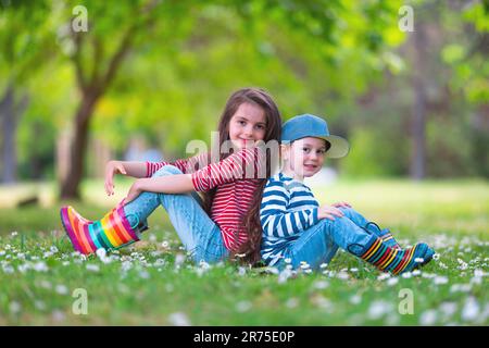 Fröhliche Kinder Junge und Mädchen in Gummistiefeln spielen draußen im grünen Park mit blühenden Blüten Stockfoto