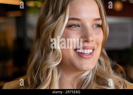 Glückliche weiße Geschäftsfrau in Übergröße mit langen blonden Haaren, die wegsieht und im Büro lächelt Stockfoto