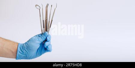 Männerhand in blauem Handschuh, die Zahnwerkzeuge auf Weiß hält Stockfoto