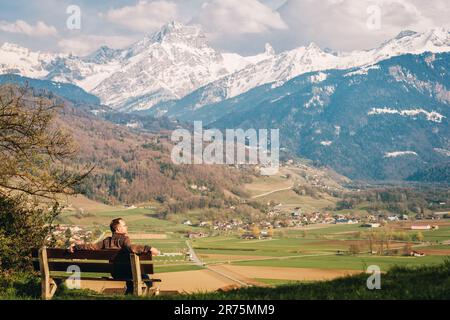 Ein Mann entspannt auf der Bank, bewundert die schweizer Alpen im Kanton Wallis, Schweiz Stockfoto