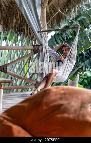 Nordamerika, Karibik, Großantillen, Hispaniola, Dominikanische Republik, Provinz Sama, Halbinsel Sama, El Limón, hübsche Frau, die in einem Hängestuhl in der Sama Eco Lodge sitzt und einen Mojito trinkt Stockfoto