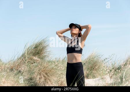 Sportliche Läuferin in Sanddünen mit den Händen am Kopf Stockfoto