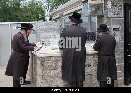 Vier jüdische Männer beten am Grabstein des Ribnitz Rebbe, da man annimmt, dass Gebete in der Nähe der Gerechten verstärkt werden. In Monsey New York. Stockfoto