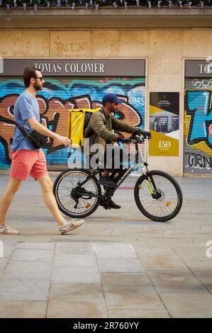 Barcelona - 12. Juni 2023: Glovo Liefermann auf einem Fahrrad, der durch die engen Gassen von Barcelona verteilt wird Stockfoto