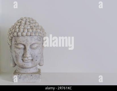 Nahaufnahme der keramischen Statuette eines Buddha-Kopfes auf grauem Hintergrund mit Kopierbereich. Stockfoto