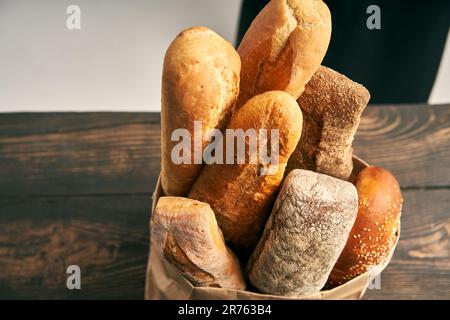 Draufsicht verschiedener Arten französischer Brotbaguettes in Papiertüte auf Holzhintergrund. Bäckerei, köstliches Speisenkonzept Stockfoto