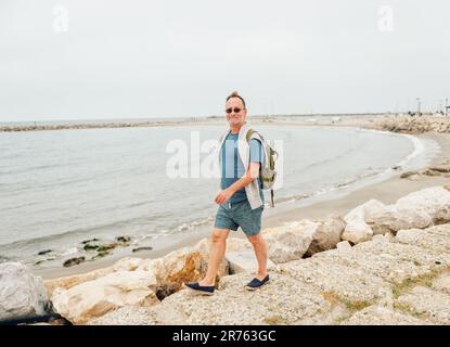 Mann, der Sommerurlaub am Meer genießt, trägt gestreiftes nautisches T-Shirt und Rucksack. Bild aufgenommen in Saintes-Maries-de-la-Mer, Hauptstadt der Camargue, S. Stockfoto