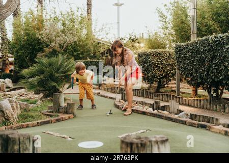 Gruppe von zwei lustigen Kindern, die Minigolf spielen, Kinder genießen Sommerurlaub Stockfoto