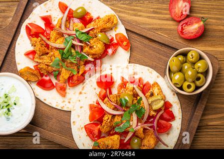 Kochen traditioneller griechischer Gerichte Gyros: Nahaufnahme von Pita-Brot mit Gemüse, Fleisch, Kräutern, Oliven auf rustikalem Holzbrett mit Tzatziki-Sauce Stockfoto