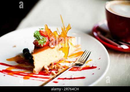 Ein köstlich aussehender Kuchen mit Erdbeerscheiben und einem Nieselregen Sirup auf einem weißen Teller Stockfoto