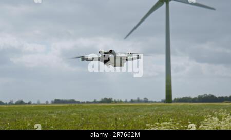 OSTFRIESIEN, DEUTSCHLAND - 25. MAI 2023: Kamera Drohne DJI Mini 3 Pro schwebt in der Luft in der Nähe eines Feldes mit Windturbinen Stockfoto