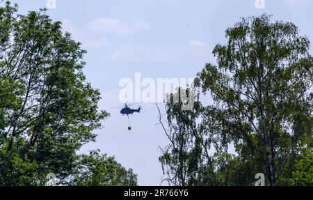 13. Juni 2023, Mecklenburg-Vorpommern, Lübtheen: Ein Helikopter der Bundespolizei wirft Feuerlöschwasser ab, um einen Waldbrand in einem ehemaligen munitionsverseuchten Ausbildungsgebiet zu bekämpfen. Am 12. Juni 2023 brachen Brände in zwei ehemaligen Ausbildungsgebieten im Südwesten Mecklenburgs aus. Foto: Jens Büttner/dpa Stockfoto